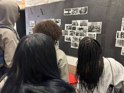 Students looking at a wall of black-and-white photographs pinned to a dark board during a class exhibition