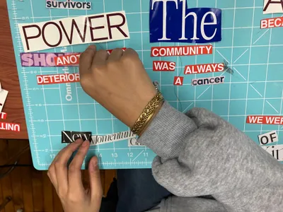 A student's hands arranging cut-out magazine words on a cutting mat to build a collage poem, with fragments including "power", "survivors" and "the community"