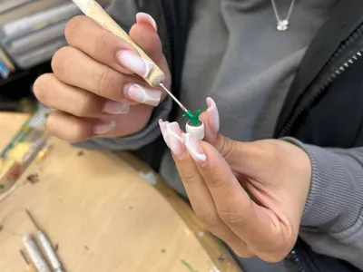Close-up of a student's hands painting a tiny clay sculpture of a potted plant with a fine brush