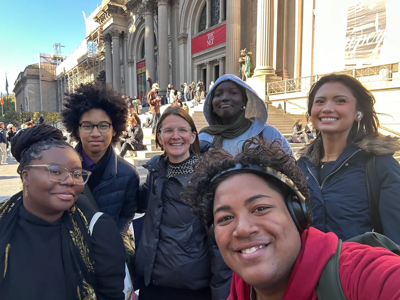 A student taking a selfie with classmates and a teacher on the steps of the Metropolitan Museum of Art