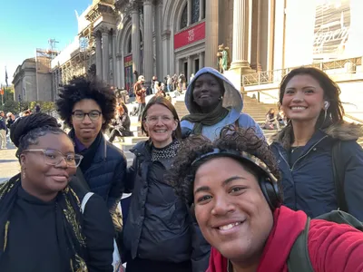 A student taking a selfie with classmates and a teacher on the steps of the Metropolitan Museum of Art