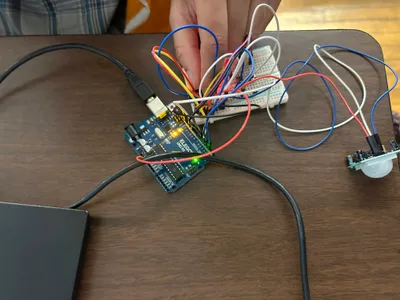 A wired Arduino circuit on a desk with a breadboard and motion sensor, a student adjusting the connections