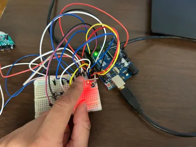 A student pressing a button on a breadboard to light a red LED, wired to an Arduino board on the desk