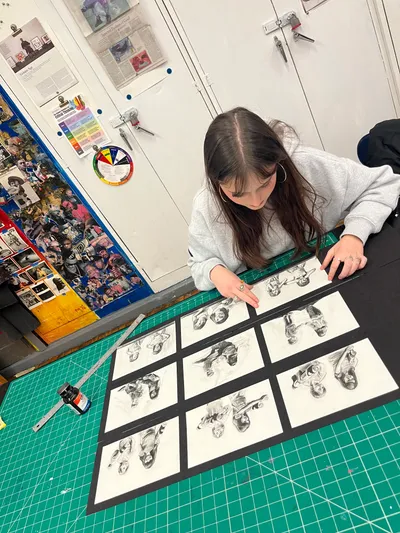 A student laying out nine mounted charcoal portrait studies on a cutting mat, arranging the series for presentation