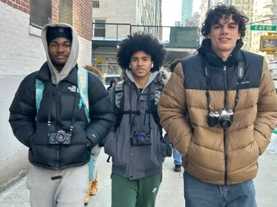 Three students in winter coats standing on East 67th Street, each with a 35mm film camera hung around their neck, ready for a photography assignment in the city