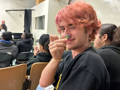 A student turning to the camera with a wry smile, balancing a small badge on his nose, during an assembly in the theatre