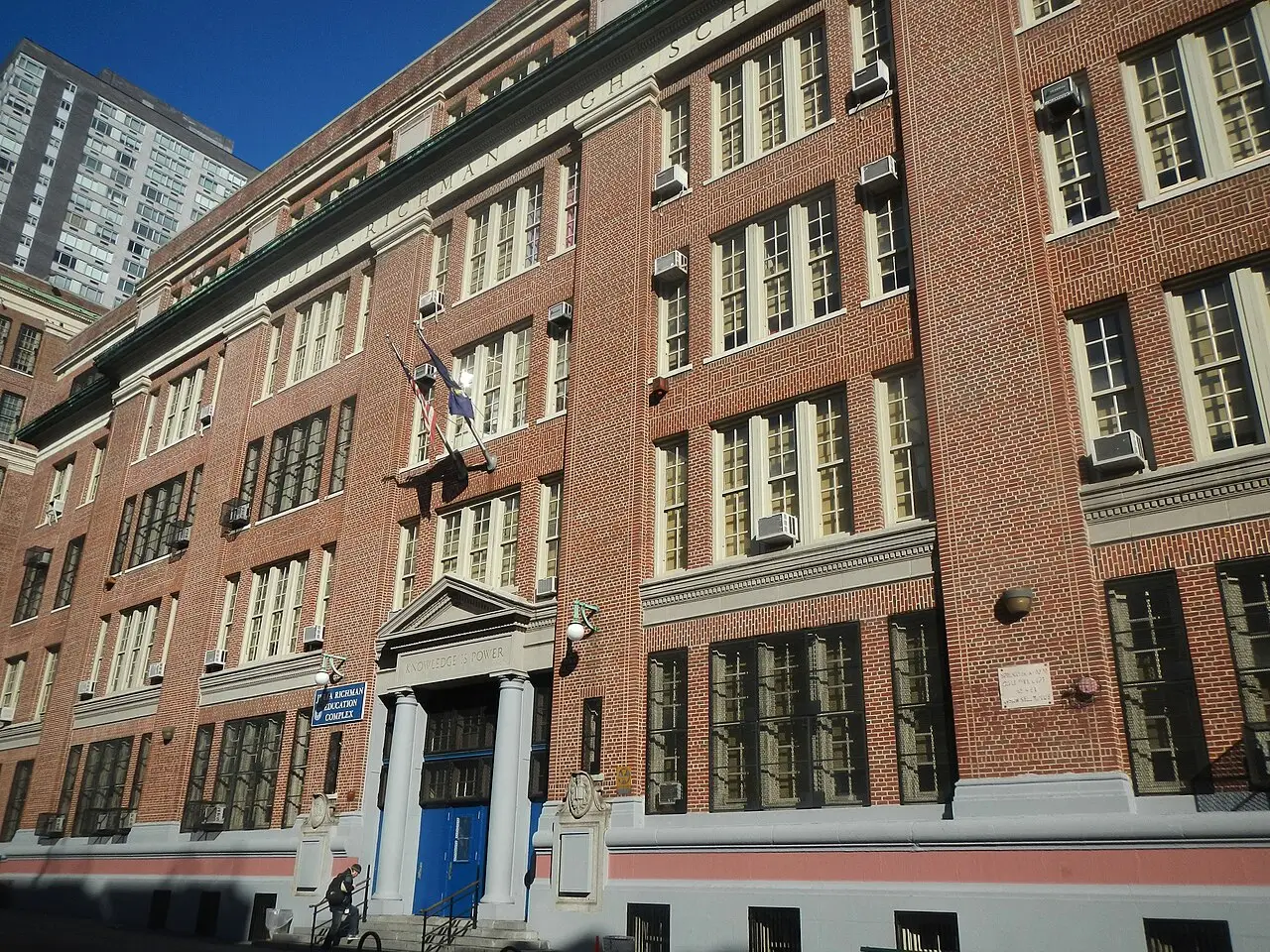 The red-brick facade of the Julia Richman Education Complex, with a blue sign beside the columned entrance and the words "Knowledge is Power" carved into the stone pediment above the doors