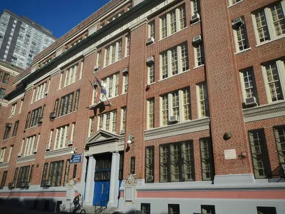 The red-brick facade of the Julia Richman Education Complex, with a blue sign beside the columned entrance and the words "Knowledge is Power" carved into the stone pediment above the doors