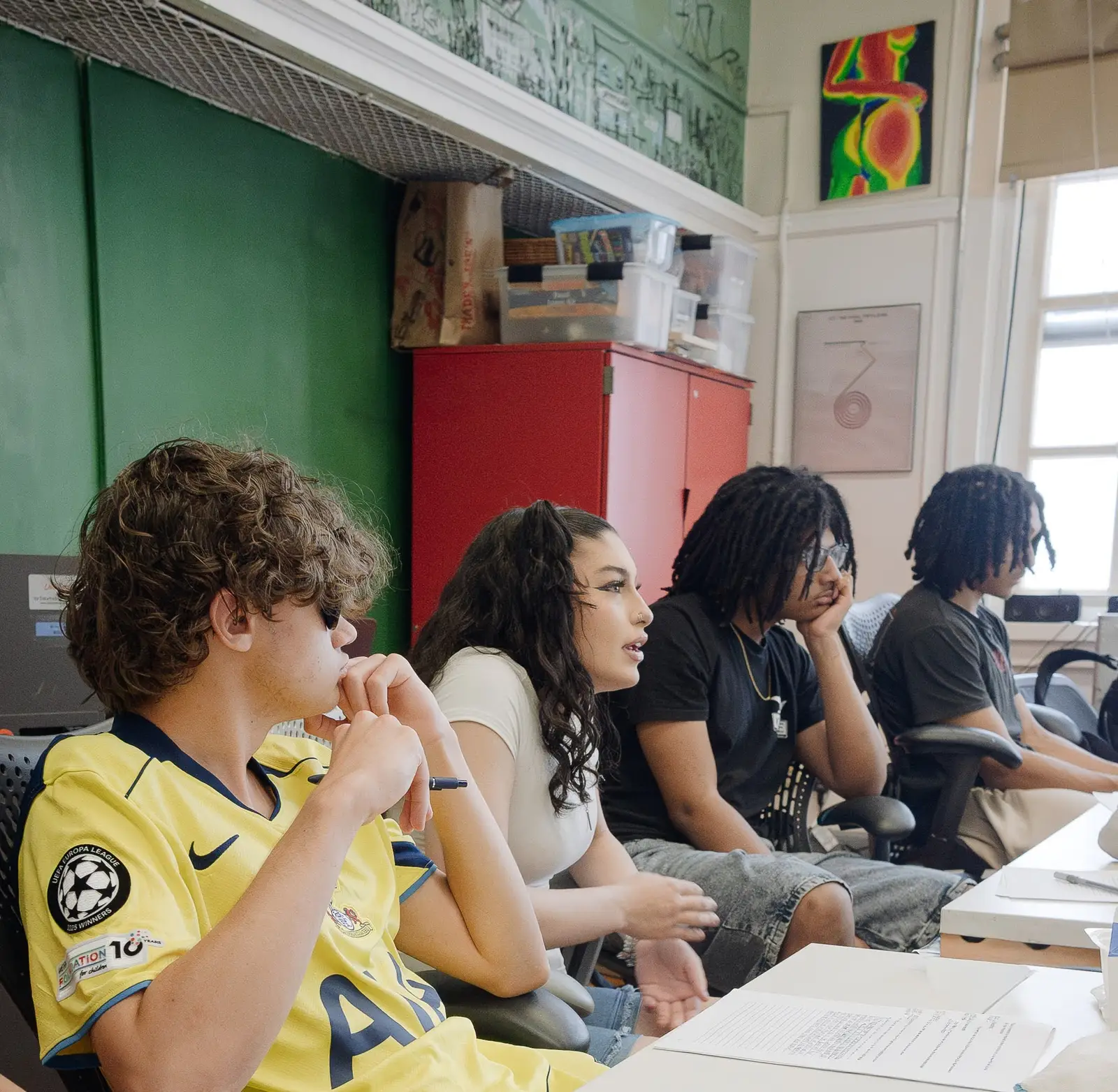 Four students of different ages sitting in a row, listening intently during a class discussion