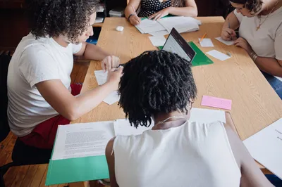 Students seated around a table from above, annotating printed readings and marking up a text together